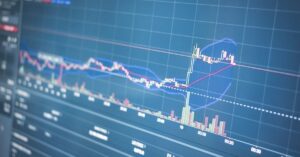 Stock chart on a blue grid with candlestick candles, moving averages, and volume bars at the bottom.